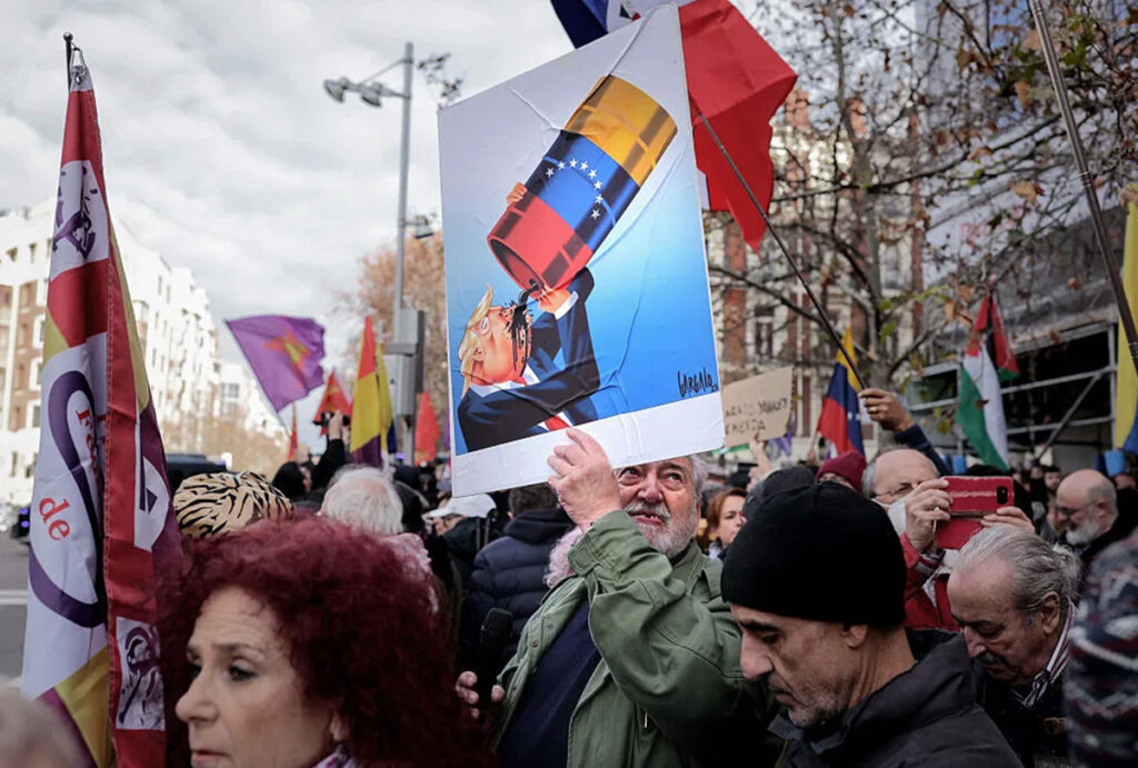 a madrid protestor holds a caricature of donald trump drinking from a venezuelan oil barrel by portuguese cartoonist vasco gargalo 1200x810
