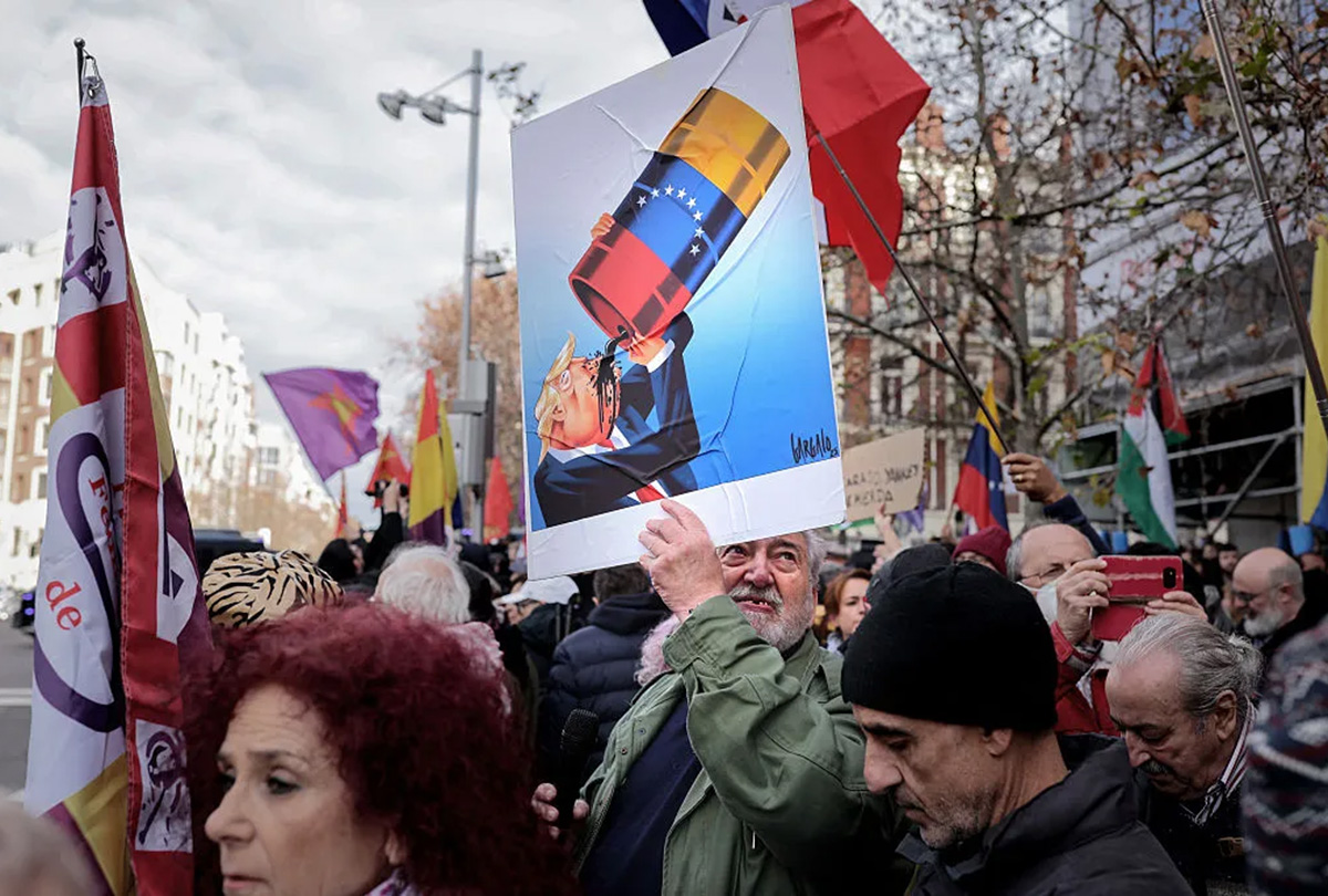 a madrid protestor holds a caricature of donald trump drinking from a venezuelan oil barrel by portuguese cartoonist vasco gargalo 1200x810