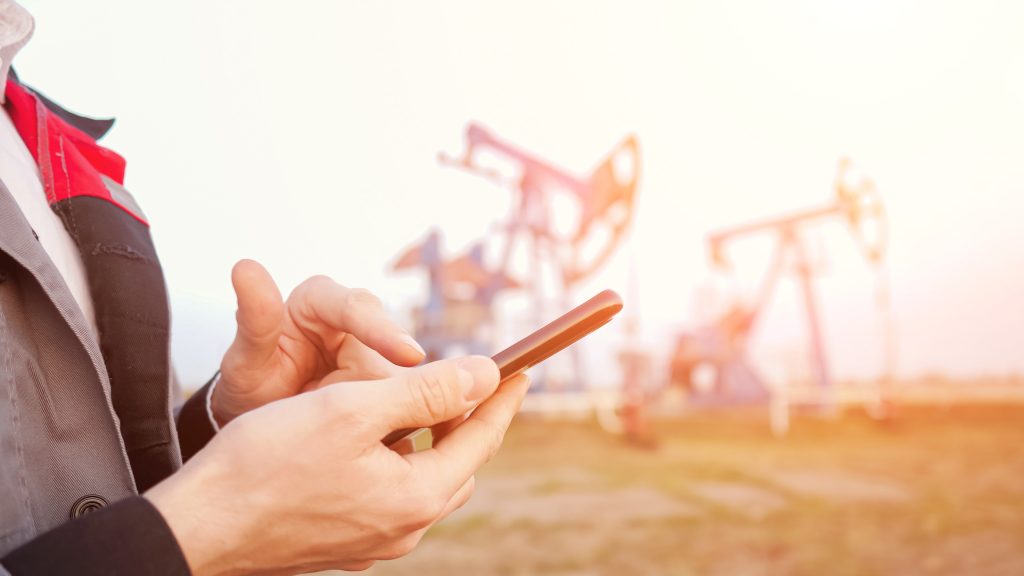 Close-up of a male hand in uniform with a phone on the background of pumping oil