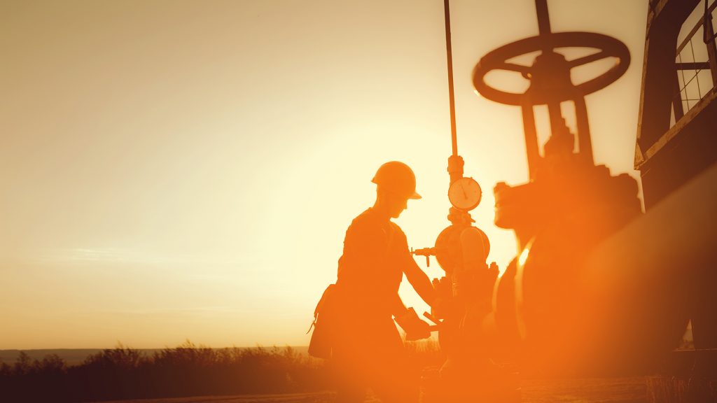 oil worker is checking the oil pump on the sunset background.